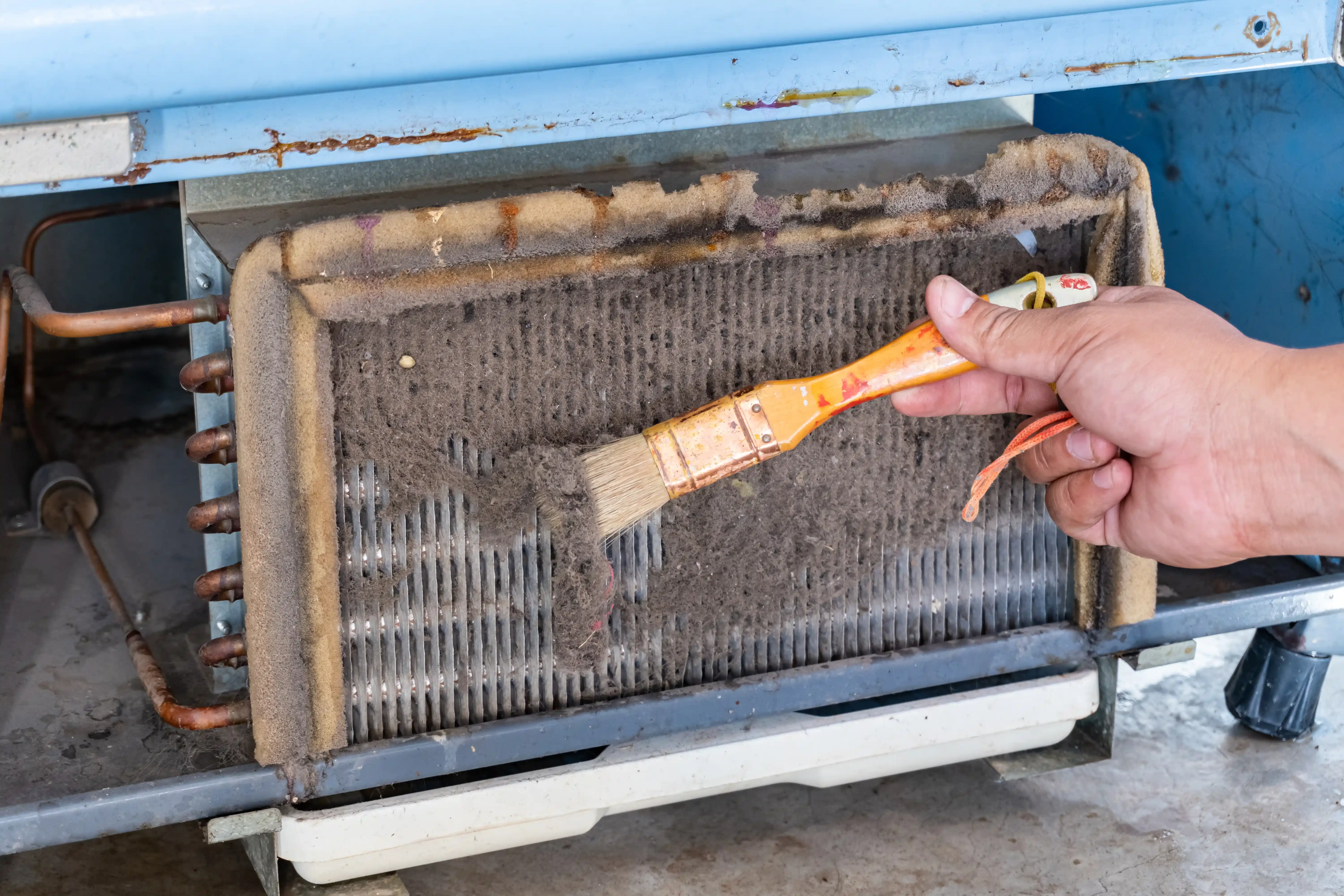 An Air Dynamics of Tulsa technician cleaning a heavily clogged evaporator coil as part of an AC maintenance service in Tulsa, OK.